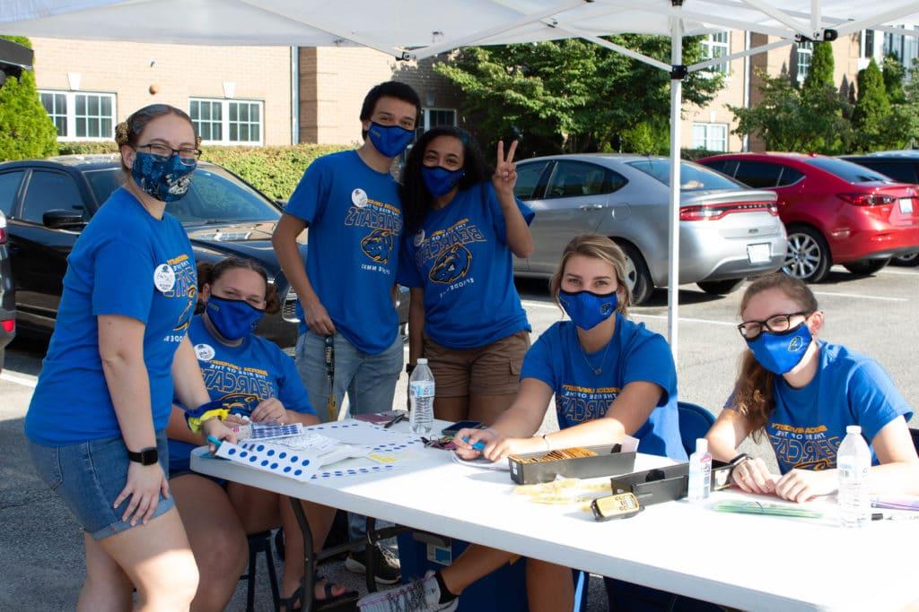 学生小组, wearing blue masks and matching blue shirts, are at a table outside for Orientation